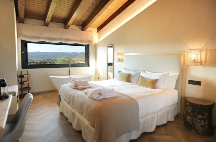 Sunlit suite at Habitat Cigueña Negra with king bed, exposed wood beams, freestanding bath, and valley views.