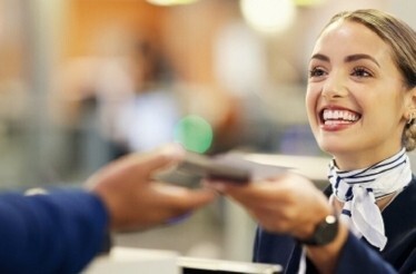 Smiling airport agent receiving travel documents from a suited traveller at a Fast Track security checkpoint