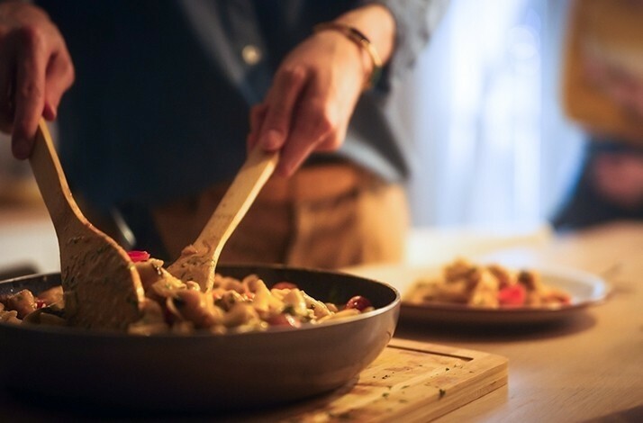A close-up view of a person using wooden spoons to mix a dish in a frying pan.
