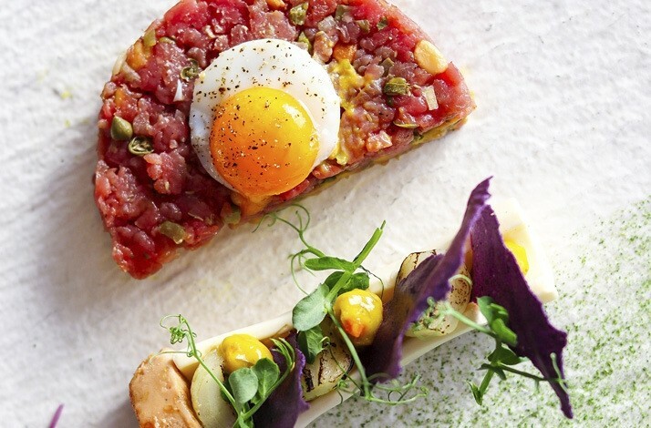 Gourmet dish featuring beef tartare, quail egg, and artistic plating