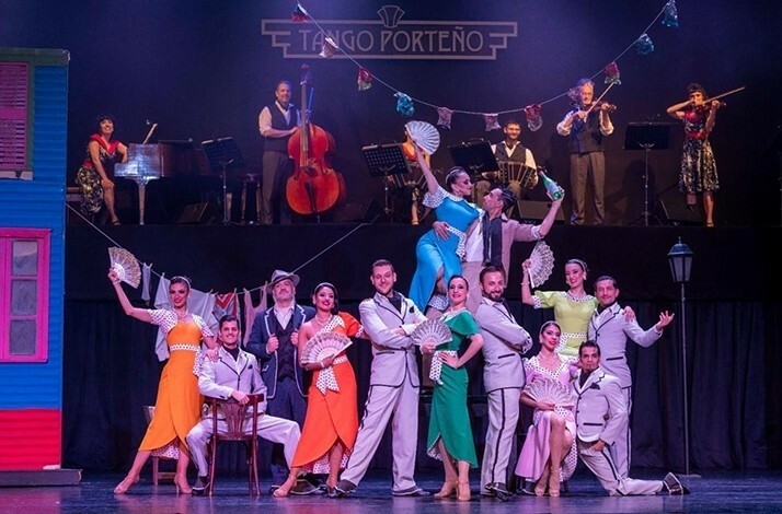 A lively tango scene with dancers in vibrant costumes and festive decor, backed by live musicians on stage of Tango Porteño Performing arts theater.