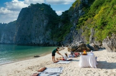 A group of people relax on a sandy beach, enjoying a picnic amidst towering limestone karsts at Hạ Long Bay's Heritage Line.