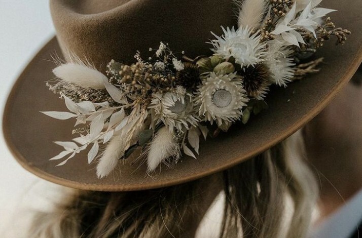 A brown hat featuring a rustic floral arrangement with white and earthy tones