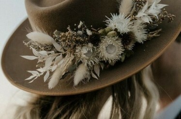 A brown hat featuring a rustic floral arrangement with white and earthy tones