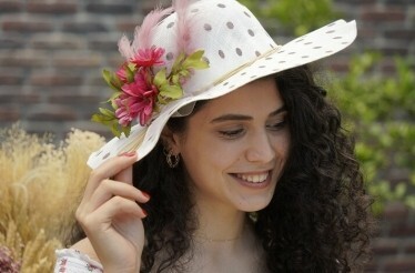 A person wearing stylish polka dot hat decorated with pink flowers and feathers
