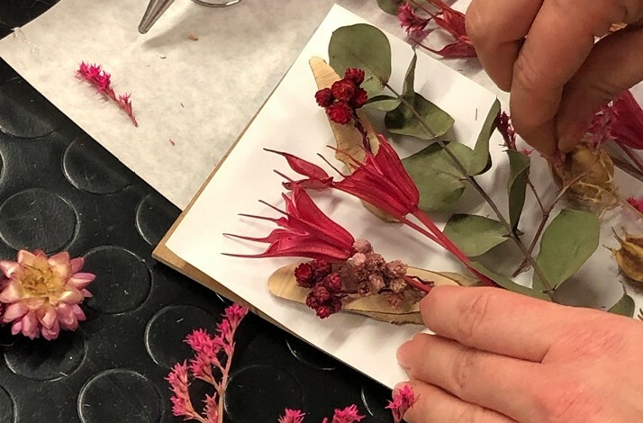 Hands arranging vibrant dried flowers and leaves on a white backdrop