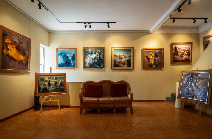 A cozy art gallery featuring abstract paintings and landscapes with a wicker sofa centerpiece
