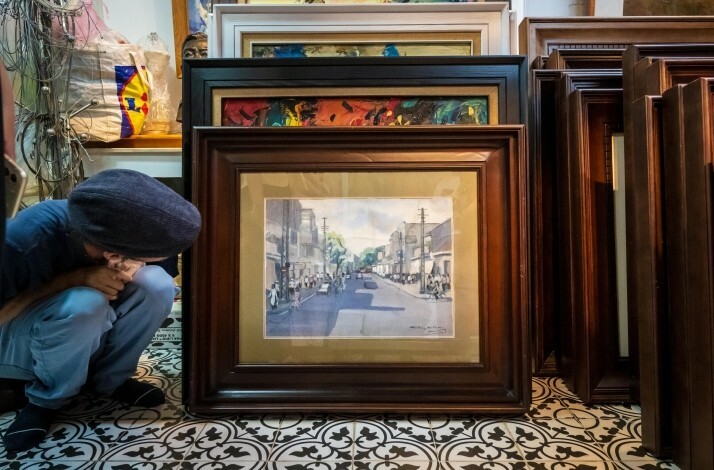 Framed watercolor of a street scene among stacked artwork and frames in a workshop setting
