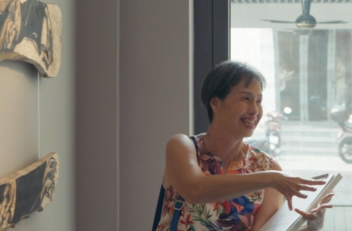 Angeline Gong is pointing at art pieces mounted on a wall during a gallery tour
