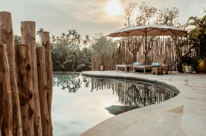 Scenic poolside with lounge chairs, umbrella, and tropical greenery at sunset
