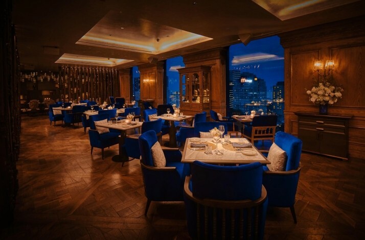 Albion Saigon restaurant's interior with tables featuring dark wooden flooring and royal blue chairs with panoramic city view.