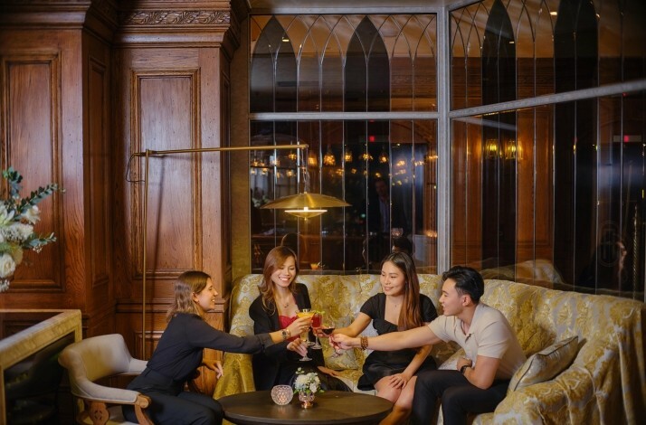 A group of four people are seated together at a couch in Albion Saigon restaurant, raising their glasses in a toast.