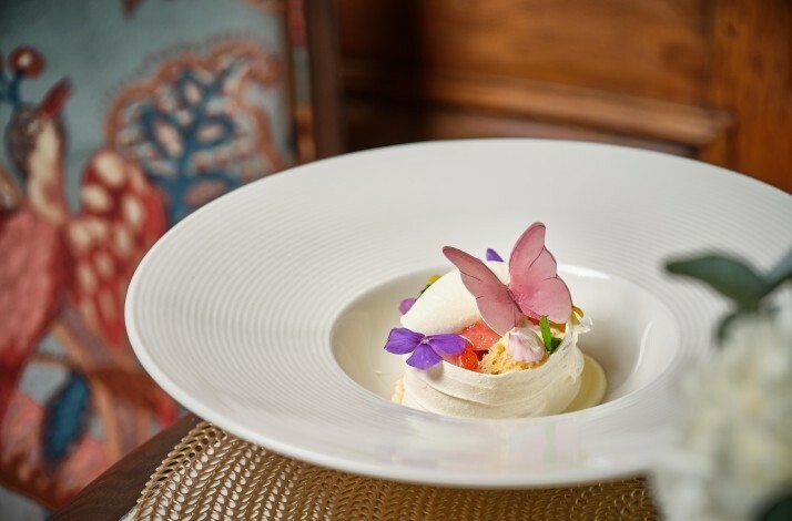 A dessert, featuring a layered meringue nest topped with fruits and edible flowers, served at Albion Saigon.