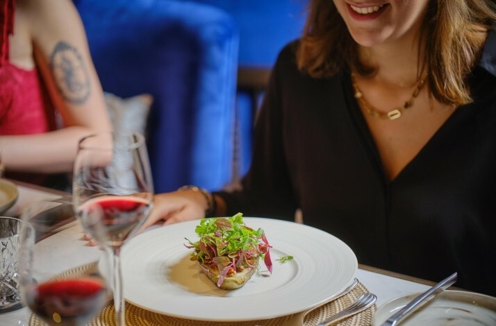 A dish served on a white plate, presented on a visitor's dine table, along with a glass of wine.