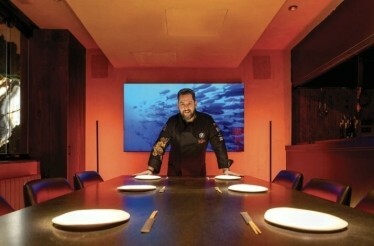 Chef Julián Mármol in a black uniform standing behind a long dining table.