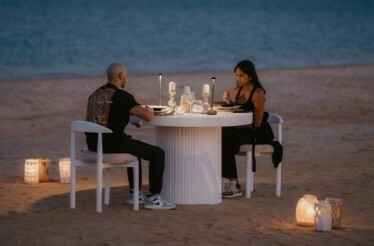 A couple at the beach enjoying a meal on a dimly lit table.