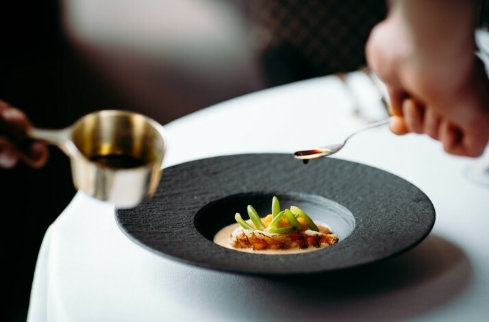 Special dish in a black plate with a souse being poured on.
