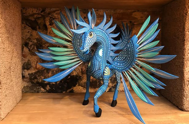 An intricate blue and green statue of a mythical winged creature stands on a wooden shelf.