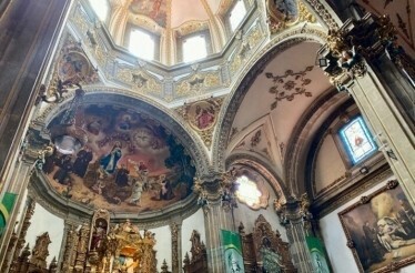 Interior of San Juan Bautista Church in Coyoacán, Mexico City, showcasing ornate domes, murals, and stained glass.