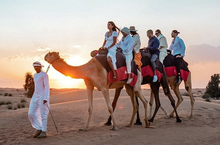 People riding camels at sunset in Dubai Desert Conservation Reserve.