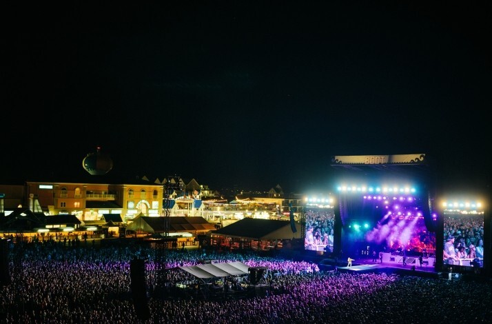 Large crowd gathers at outdoor music festival Country Calling by the waterfront, with a brightly lit stage and surrounding buildings at night.