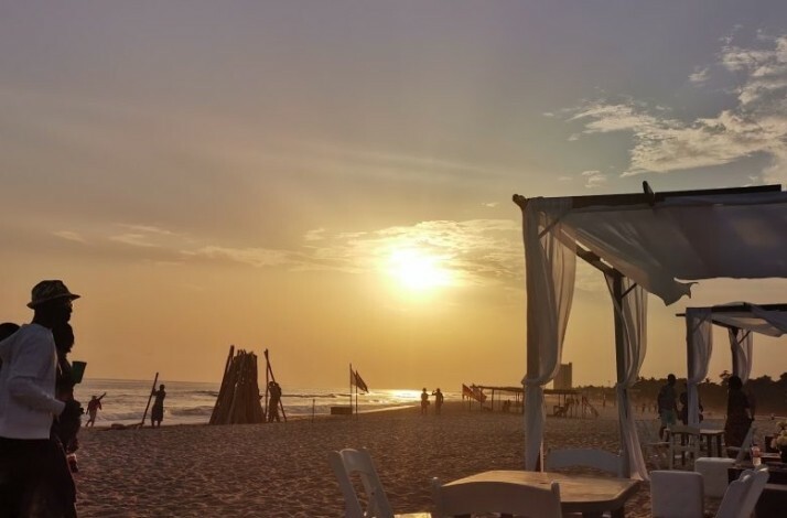 A serene sunset at a vibrant Ghanaian beach, dotted with visitors, cozy seating, and a calm ambiance.