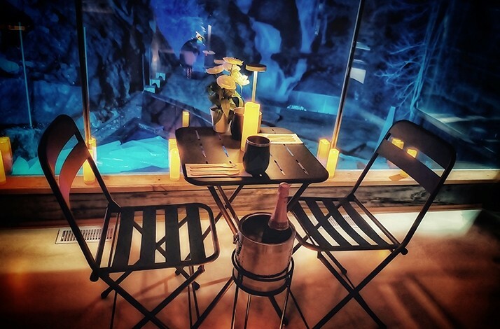 A romantic, dimly lit setting with a small table set for two, and a backdrop that suggests an icy cavern at Calumet Falls