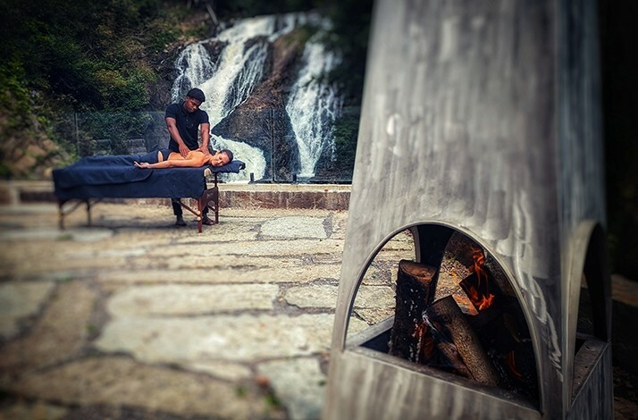 An outdoor massage session taking place near the waterfall at Calumet Falls, complemented by a cozy fireplace