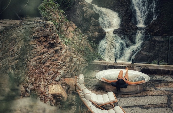A woman relaxes in a circular outdoor tub with a waterfall cascading nearby, at Calumet Falls