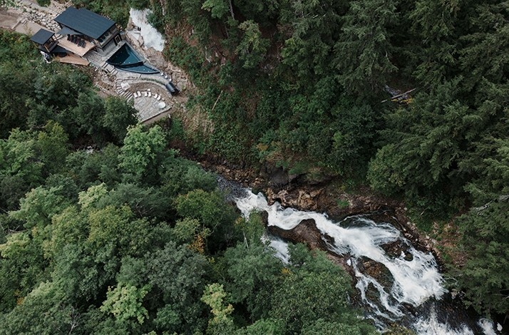 An aerial view of a secluded lodge built into a hillside, with a rushing waterfall cascading down a gorge at Calumet Falls
