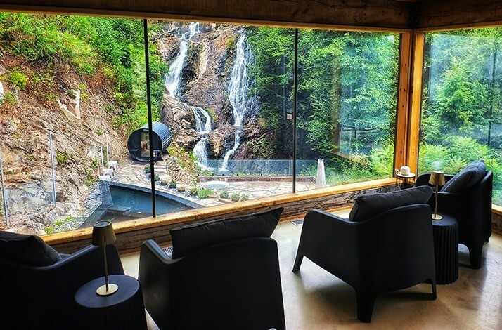 A luxurious interior with dark armchairs facing a breathtaking view of a waterfall cascading down a hillside at Calumet Falls