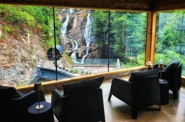A luxurious interior with dark armchairs facing a breathtaking view of a waterfall cascading down a hillside at Calumet Falls