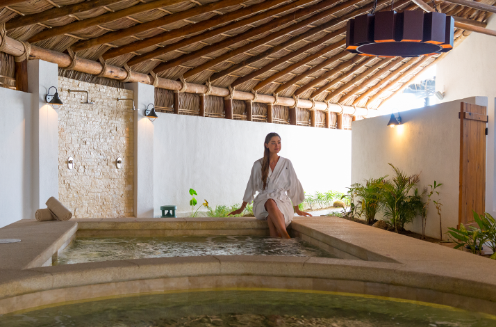 A woman in a white robe sits at the edge of a spa tub, at Hotel El Ganzo