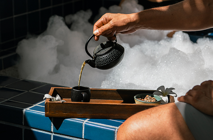 A hand pouring tea from a black teapot into a small cup, offered at Hotel El Ganzo