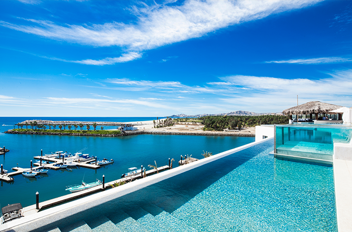 A view of a pool overlooking a coastal marina, under a vibrant blue sky at Hotel El Ganzo