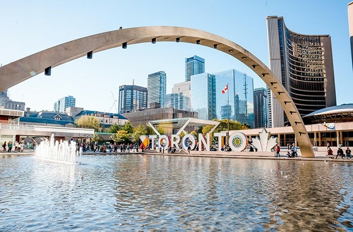 Nathan Phillips Square in Toronto, featuring the 'TORONTO' sign, a reflecting pool, and a backdrop of modern skyscrapers 
