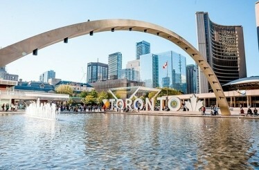 Nathan Phillips Square in Toronto, featuring the 'TORONTO' sign, a reflecting pool, and a backdrop of modern skyscrapers 
