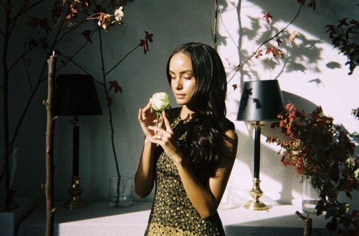 A young lady holding a flower to feel the scent in a dim room.