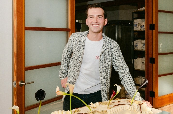 Ryan Nordheimer, a NYC-based home cook and baker, in his iconic apartment café with a cake from his curated menu served on the table.