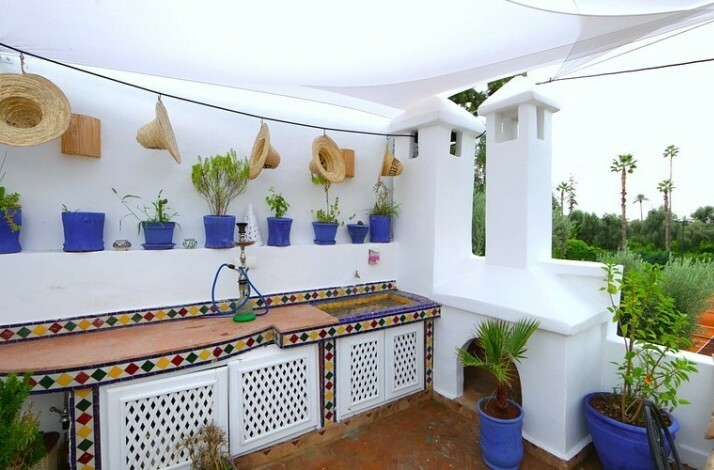 Part of the outdoor lounge/dining area of the Riad Elli Marrakech hotel with a lot of potted plants and colorful counter against white walls.