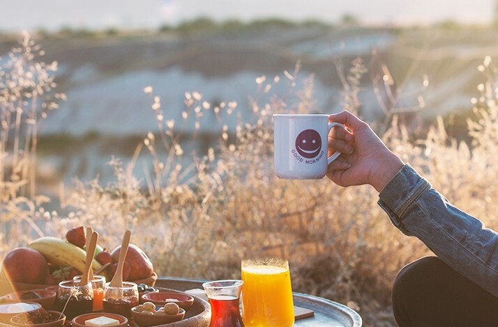 A tray with breakfast prepared by chefs from the Taskonaklar Hotel. Next to it a person with a hot cup of coffee in hand.