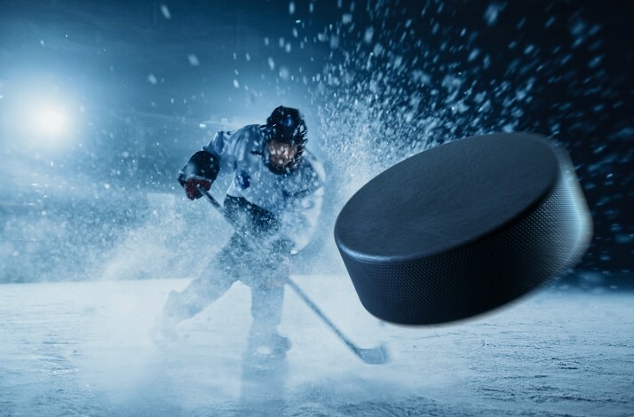 An ice hockey player hitting a hockey puck on an ice hockey field.