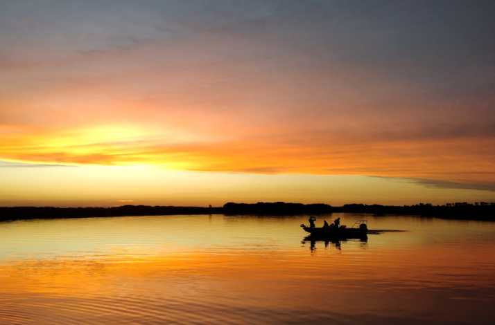 Silhouetted boat on tranquil water under a vibrant sunset sky in the Parana Delta.