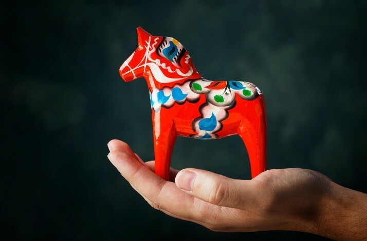 Promotional photo of a hand holding a vibrant red authentic Dala horse.