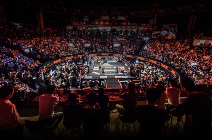 The interior of Rajadamnern Stadium filled with spectators on a Thai boxing match, as viewed from the VIP lounge.