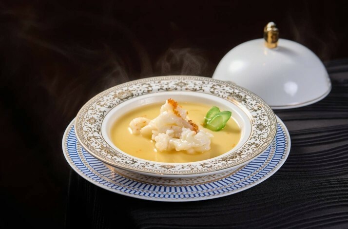 A gourmet lobster dish topped with roe served in an ornate blue and gold rimmed bowl.