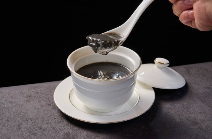 A spoonful of thick, dark dessert soup being lifted from a white porcelain tureen.