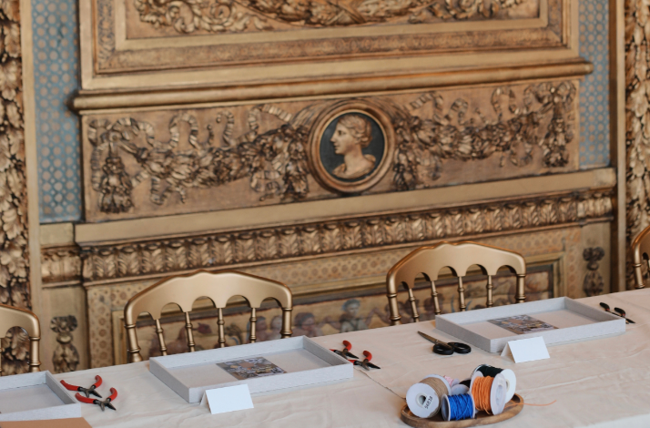 Craft workshop setup at Hôtel de Lauzun with tools, trays, and spools of thread on a long table.