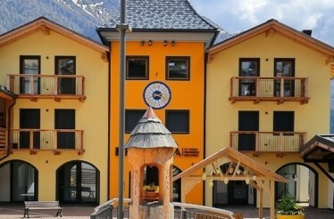 Yellow-orange alpine building with balconies and a clock.
