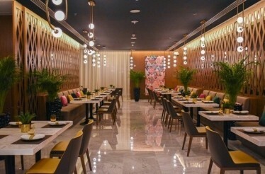 A stylish restaurant with warm lighting, marble floors, and neatly arranged tables surrounded by plants.